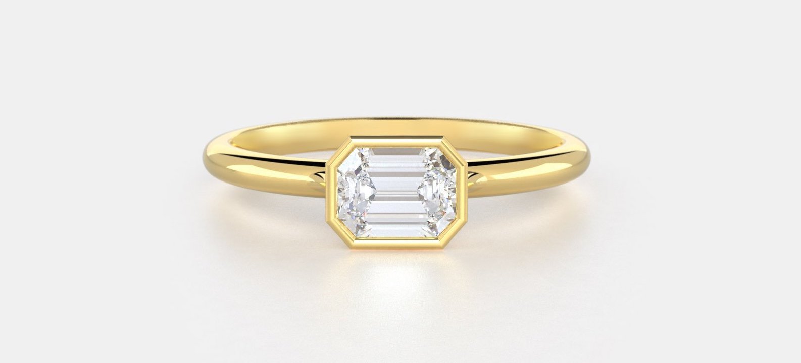 An east west bezel setting in yellow gold featuring an emerald lab grown diamond